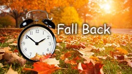 Fall Back text. An alarm clock in a field of leaves.