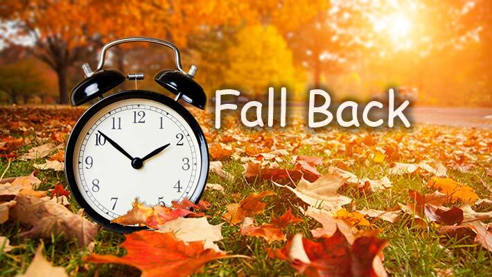 Fall Back. An alarm clock sits on a lawn full of fallen leaves.